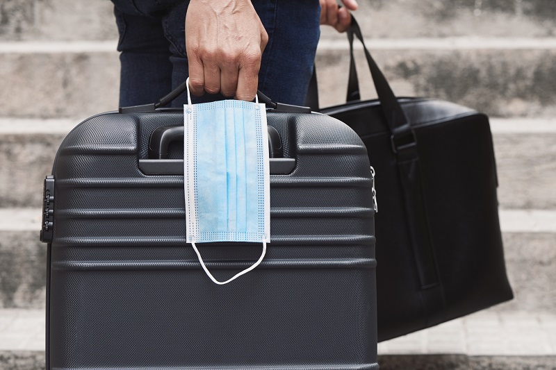 Business-Reisender hält Koffer, Tasche und Maske